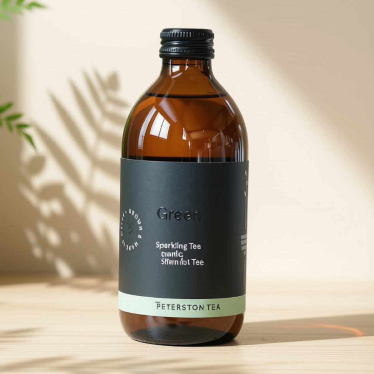 An amber glass bottle of Peterston Tea Organic Green Sparkling Tea, featuring a matte black label with white text and a light green band at the bottom, set on a light wooden surface with soft leaf shadows.